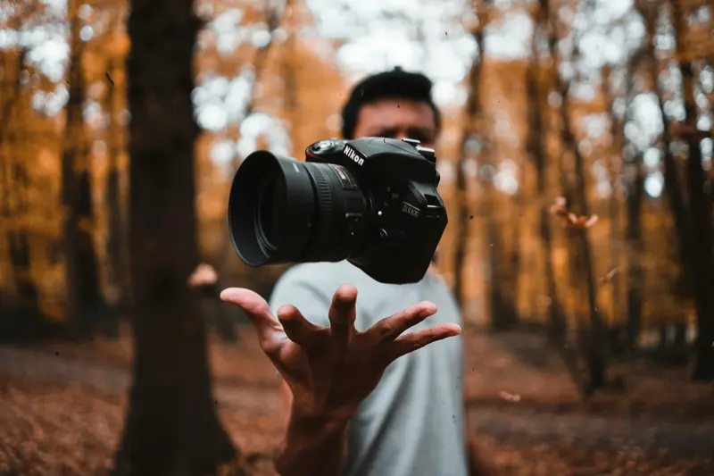 A person holding a camera up in a wooded setting