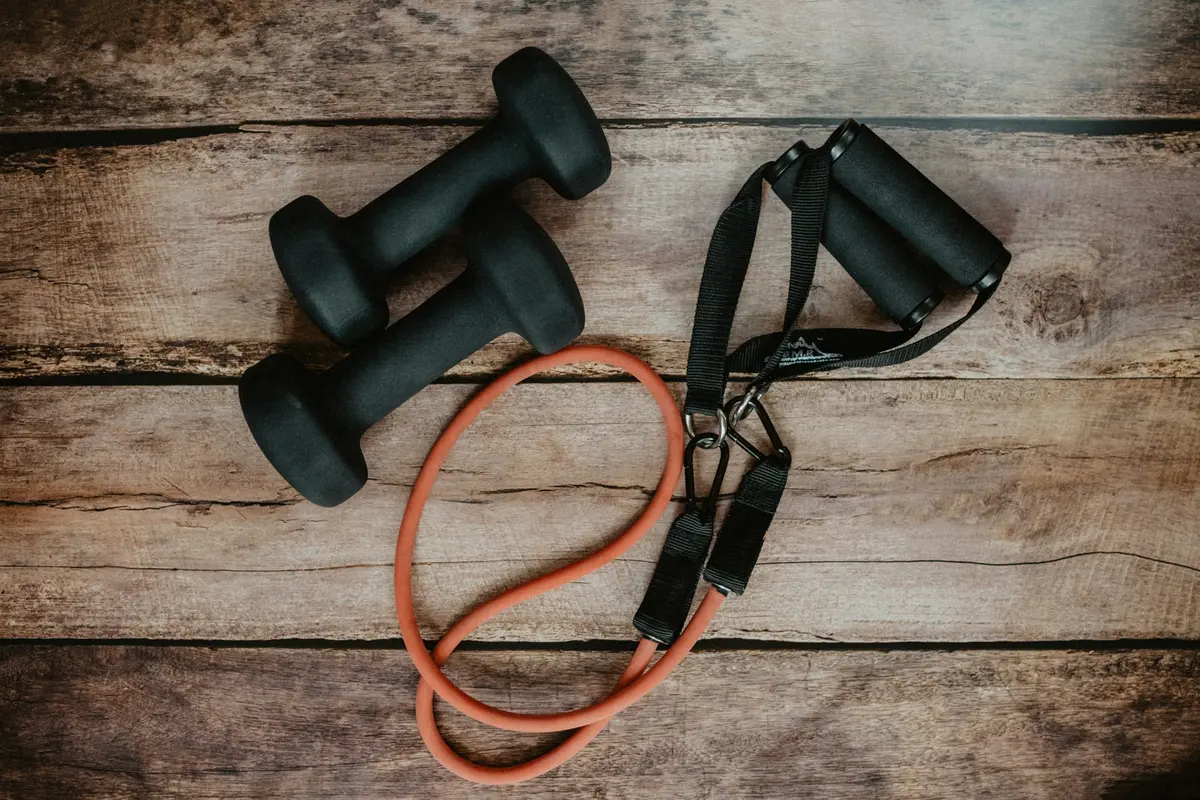 Two black dumbbells and an orange resistance band on a wooden surface