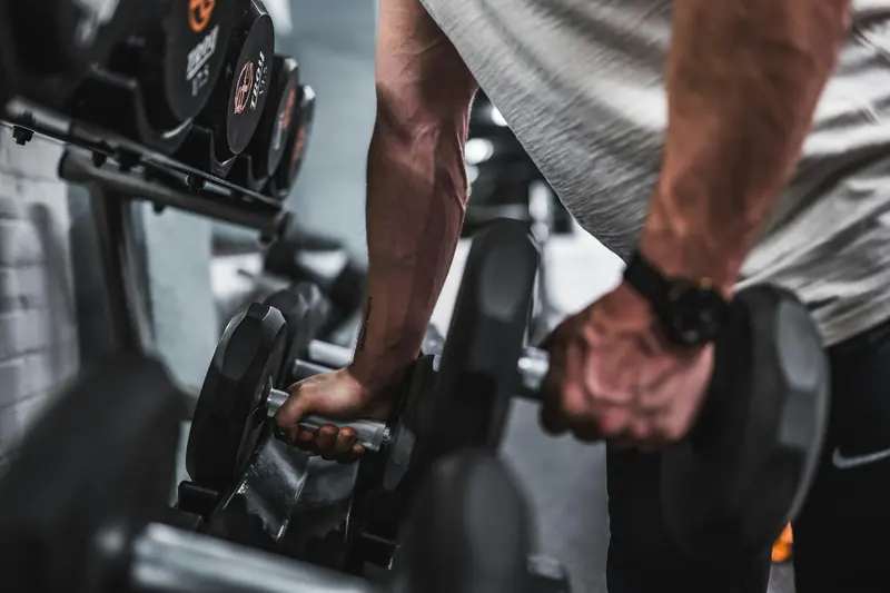 Two black dumbbells and an orange resistance band on a wooden floor