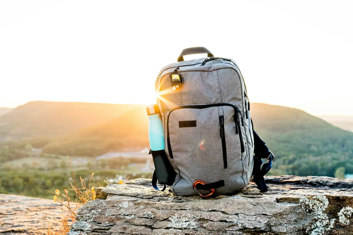 Gray and black hiking backpack with a tumbler on a rock at sunset