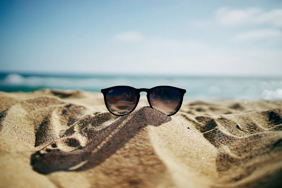 Black Wayfarer-style sunglasses on beach sand