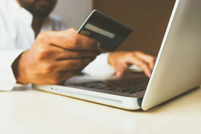 A shopper checking a card and laptop before paying